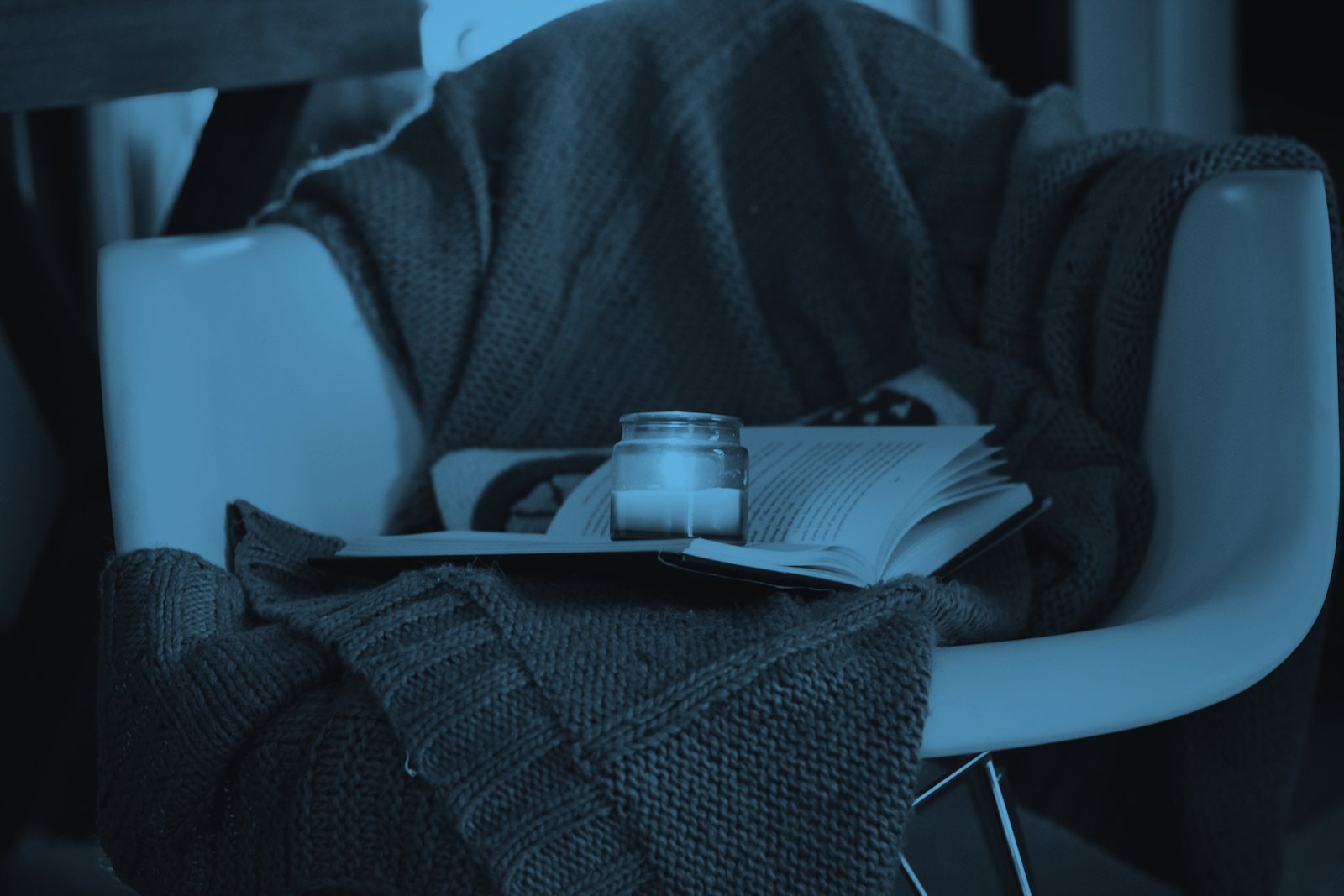A knit blanket, an open book, and a lit candle on a chair