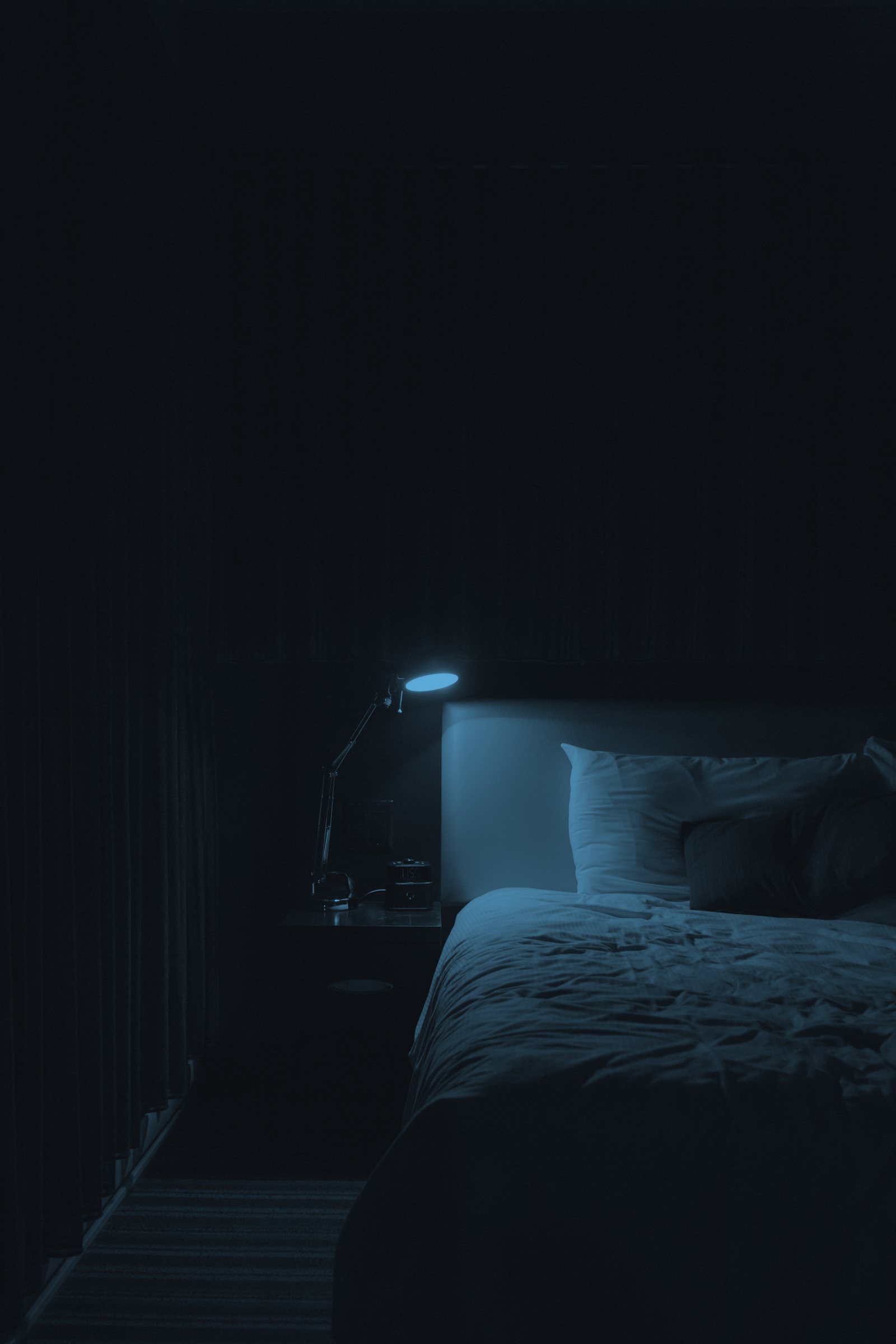 A lamp glowing beside a made bed
